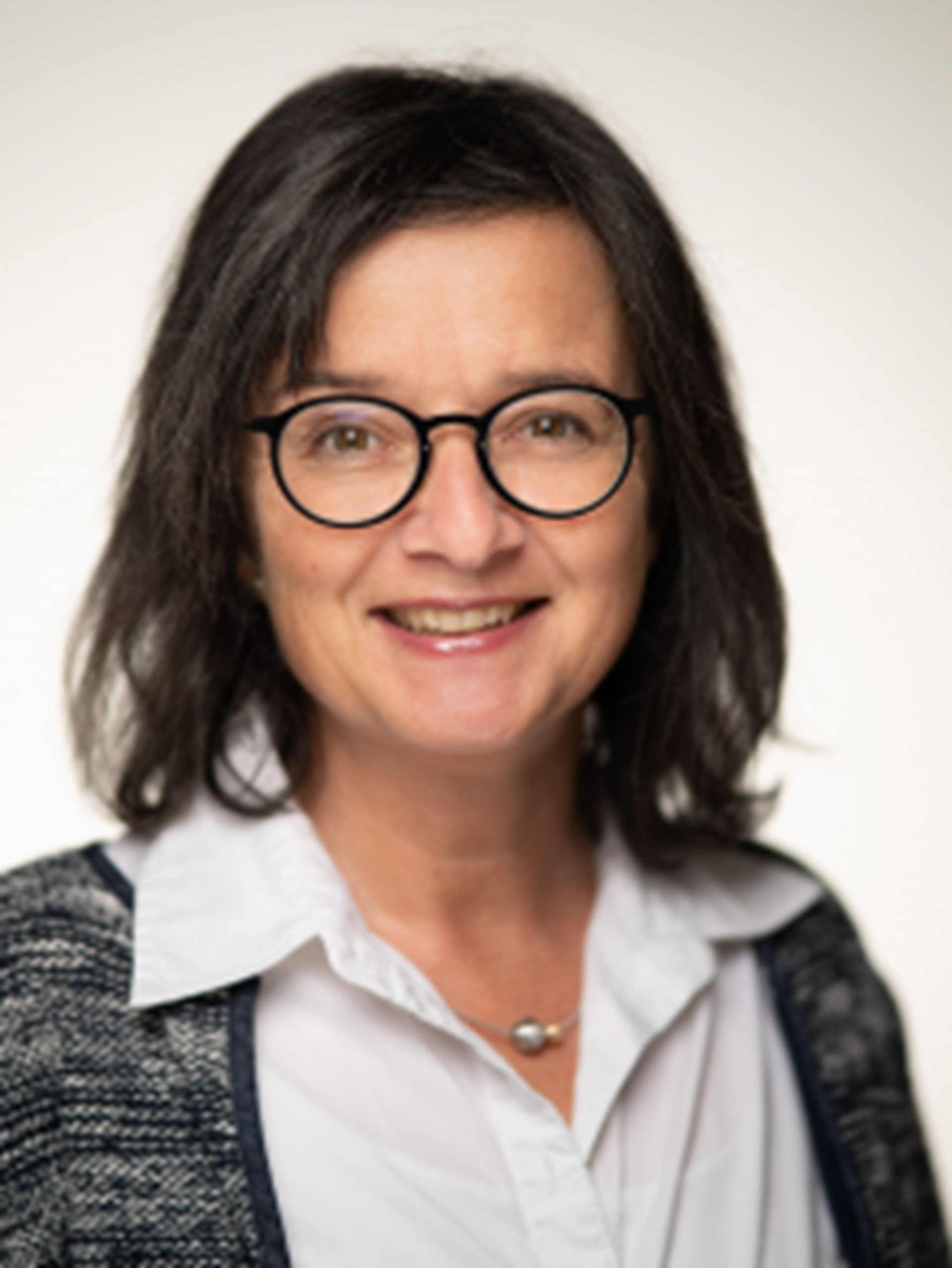 Dame lacht in die Kamera und trägt eine Brille.