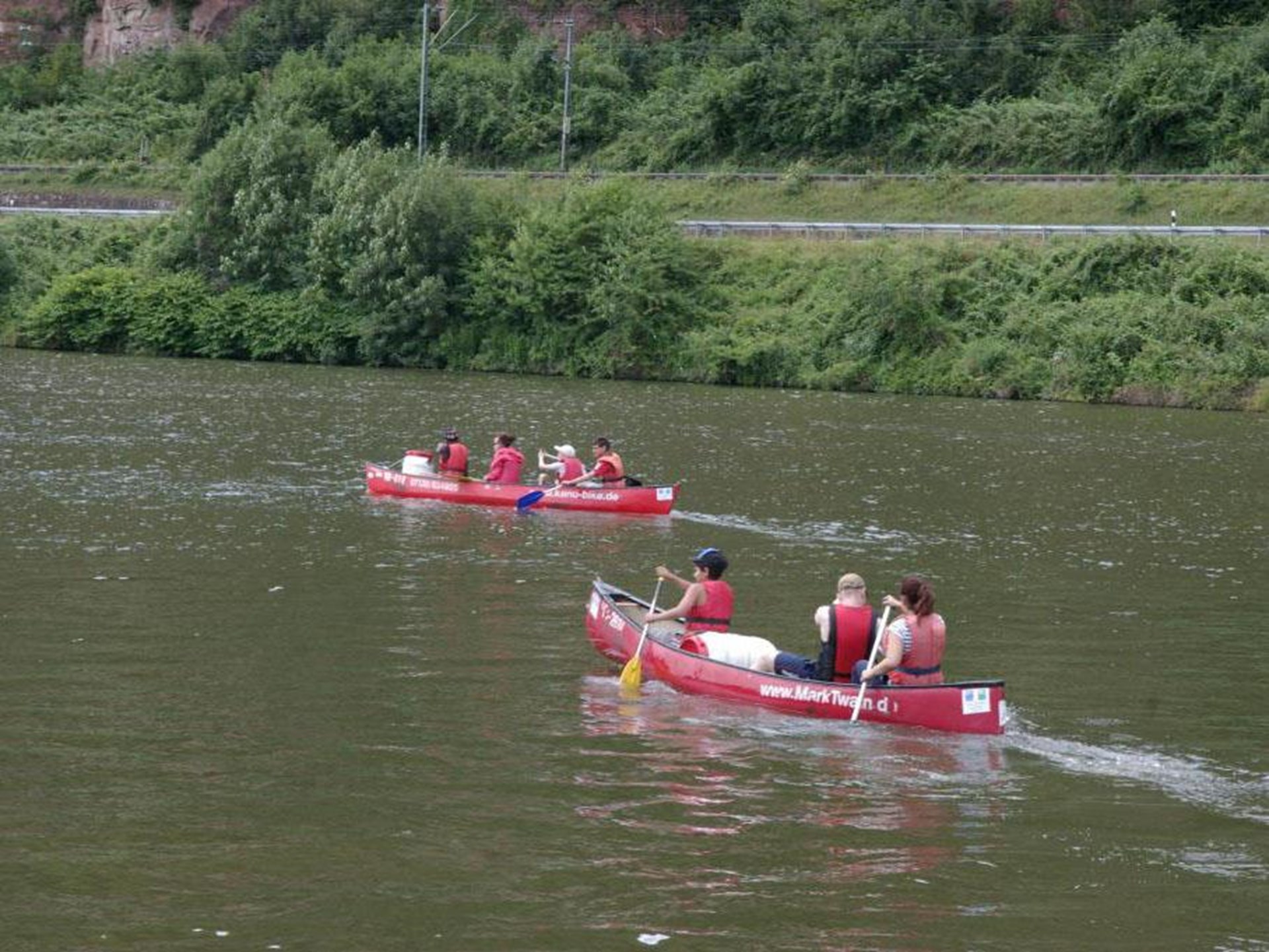 Zwei Kanus auf einem Fluss. Das Fordere ist mit vier Personen besetzt, das Hintere mit drei Personen. 